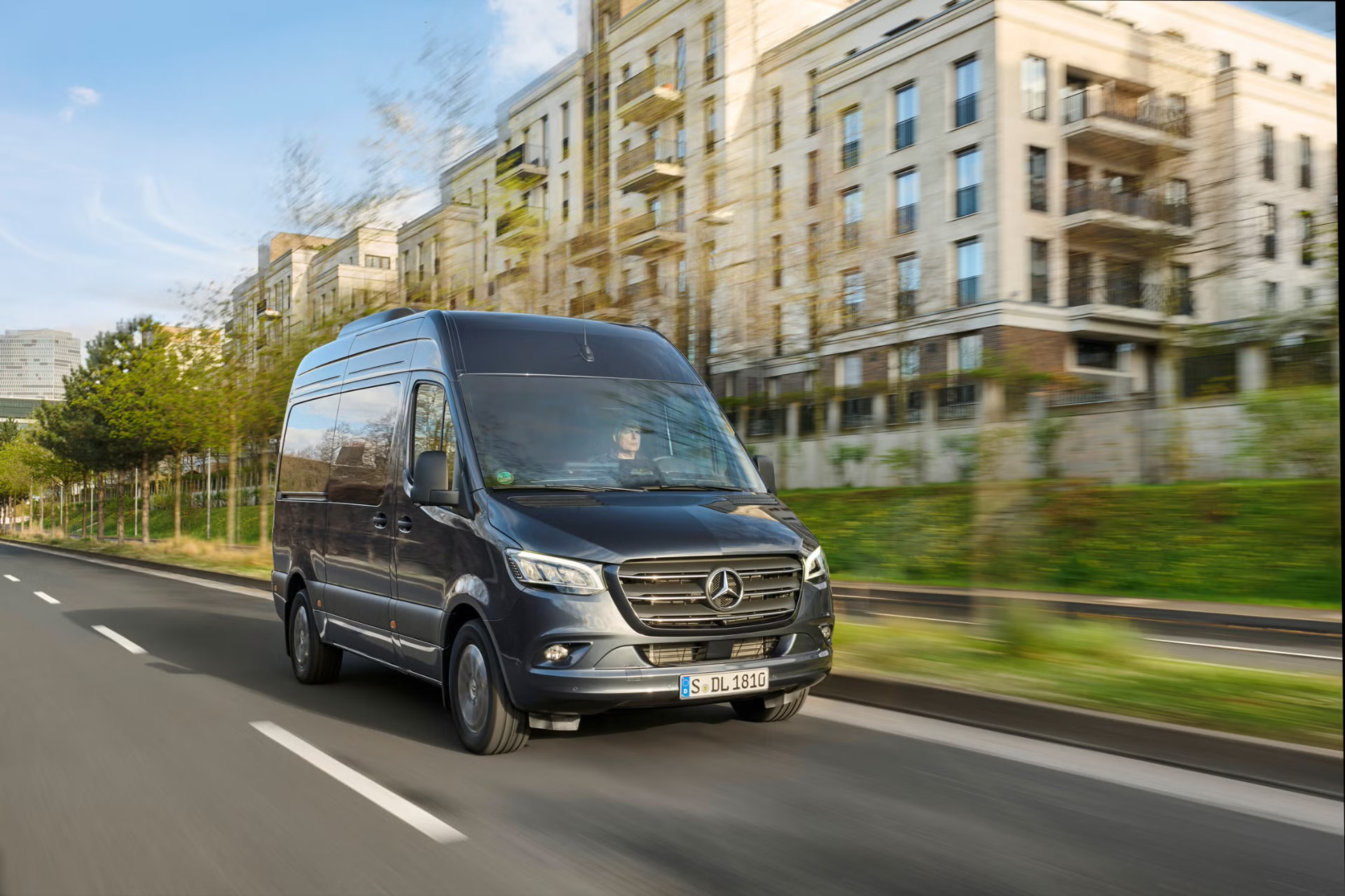 Dark Mercedes-Benz Sprinter high-roof executive van in motion along a city boulevard